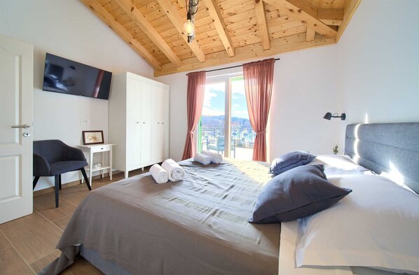 A bedroom with a large bed, a chair, a wardrobe, and a TV.