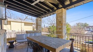 An outdoor patio with a wooden table and chairs, stone pillars, and a view of the neighborhood.