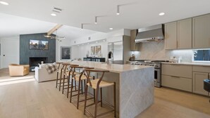 A modern kitchen with a central island, bar stools, a built-in oven, and a large window.