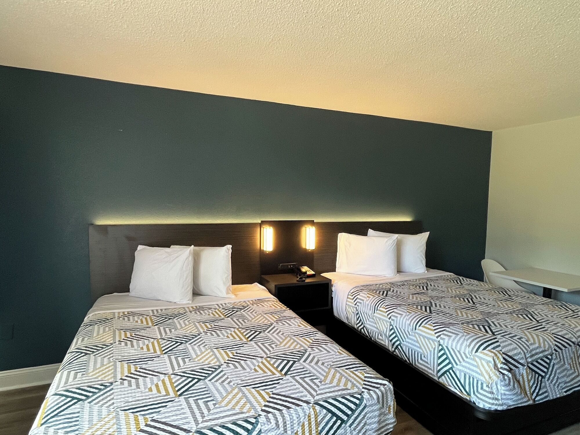 A hotel room with two single beds, a nightstand with a lamp, and a desk with a chair.