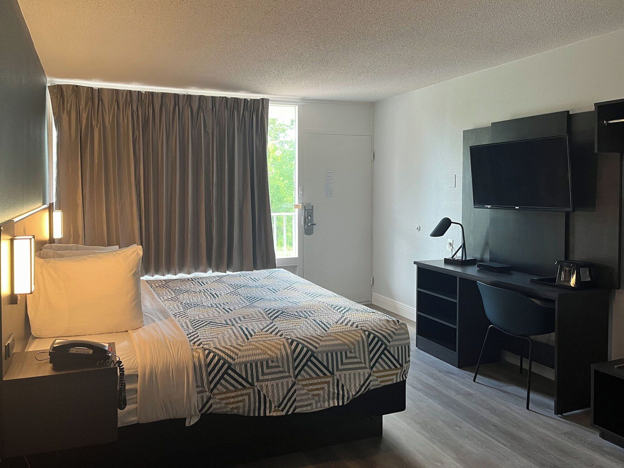 A hotel room with a bed, a desk, a television, and a window with curtains.