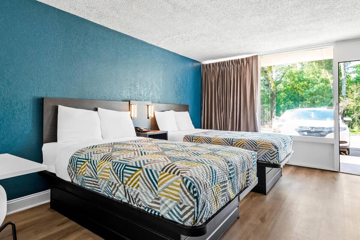 A hotel room with two beds, a desk, and a view of a car through the window.