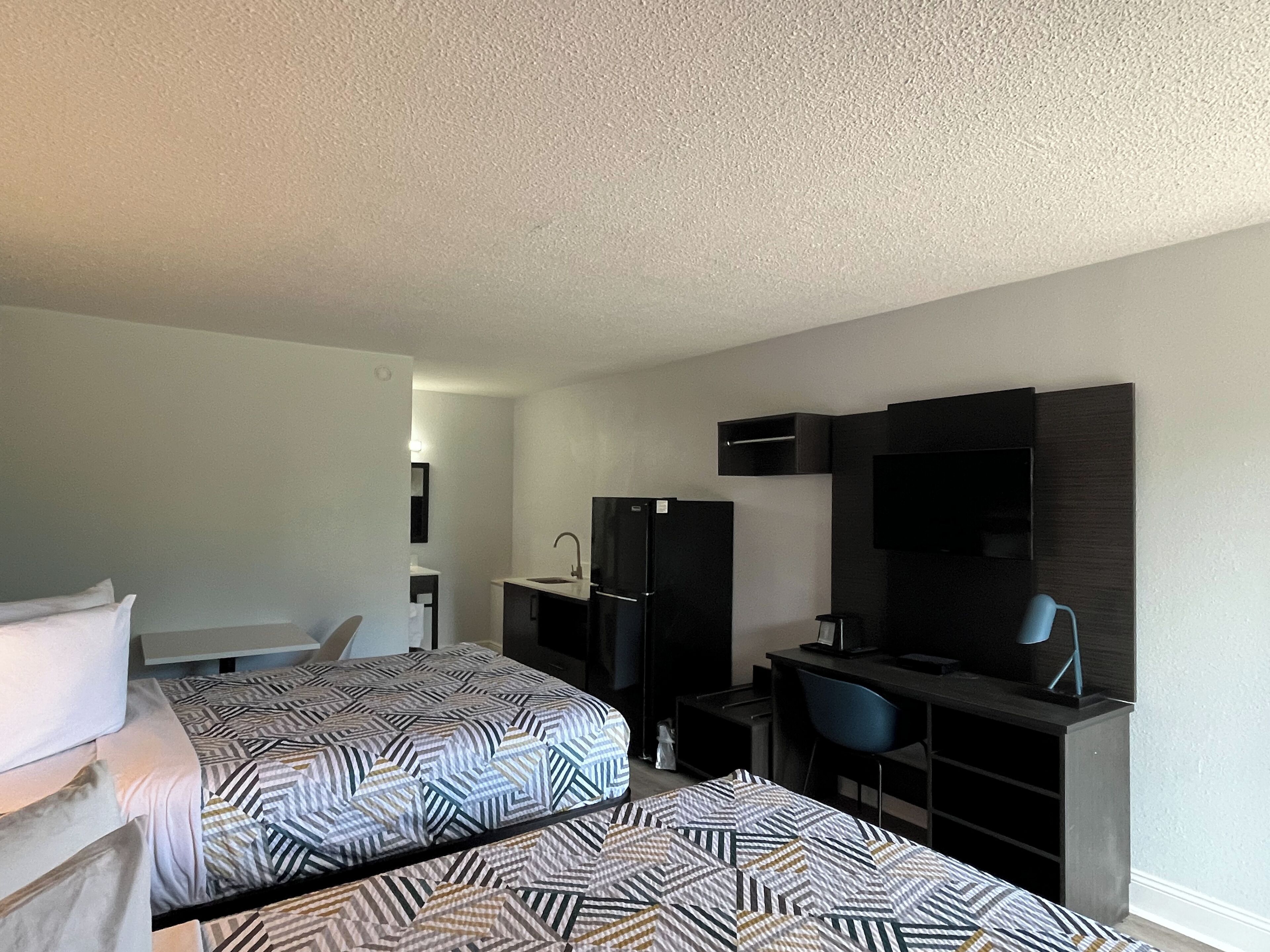 A hotel room with two beds, a desk, a chair, a TV, and a refrigerator.