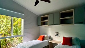 Quarto moderno com duas camas, ventoinha no teto, janela com vista para o verde e estantes embutidas.