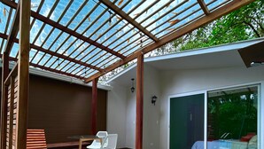 Piscina ao ar livre coberta, com um banco e cadeiras de madeira, uma mesa de jantar e uma porta de correr de vidro que dá para um quarto.