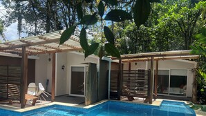 Piscina com deck de madeira e área de estar coberta.