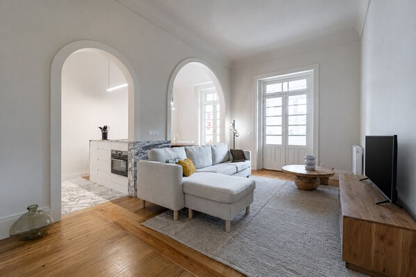 A modern living room with a sofa, a coffee table, and a TV. There are arched doorways leading to other rooms.