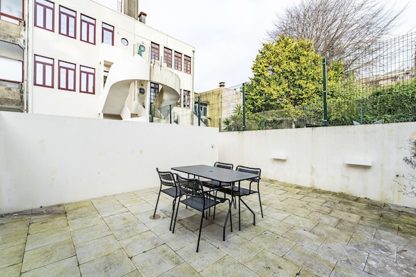 A patio with a table and chairs, a white building with red-framed windows, and a tree with yellow leaves. - Nomads Family 3BDR City Vibe Porto (Porto)