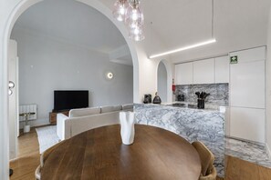 A modern living room with a wooden dining table, a sofa, and a kitchen with marble countertops. - Nomad's Family - 3BDR Charming Hideout Porto (Porto)