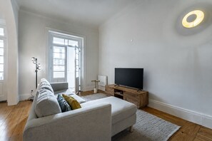 A modern living room with a sofa, a television on a wooden stand, and a floor lamp. - Nomad's Family - 3BDR Charming Hideout Porto (Porto)