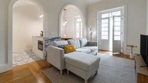 Un salon moderne avec un canapé, un téléviseur et un coin cuisine visible à travers une arche.