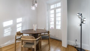 A dining area with a round table, four chairs, a vase, pendant lights, a floor lamp, and a large window with white shutters. - Nomad's Family - 3BDR Charming Hideout Porto (Porto)