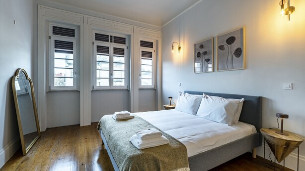 A bedroom with a bed, a bedside table, a mirror, two windows, and wall art. - Nomad's Family - 3BDR Charming Hideout Porto (Porto)