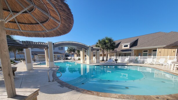 A swimming pool with a wooden deck, lounge chairs, and umbrellas.