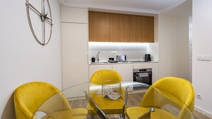A compact kitchen with wooden cabinets, a built-in oven, and a coffee machine. There is a glass dining table with yellow chairs. - Nomad's Lux - 1BDR The Silent Nest in Bonfim (Porto)