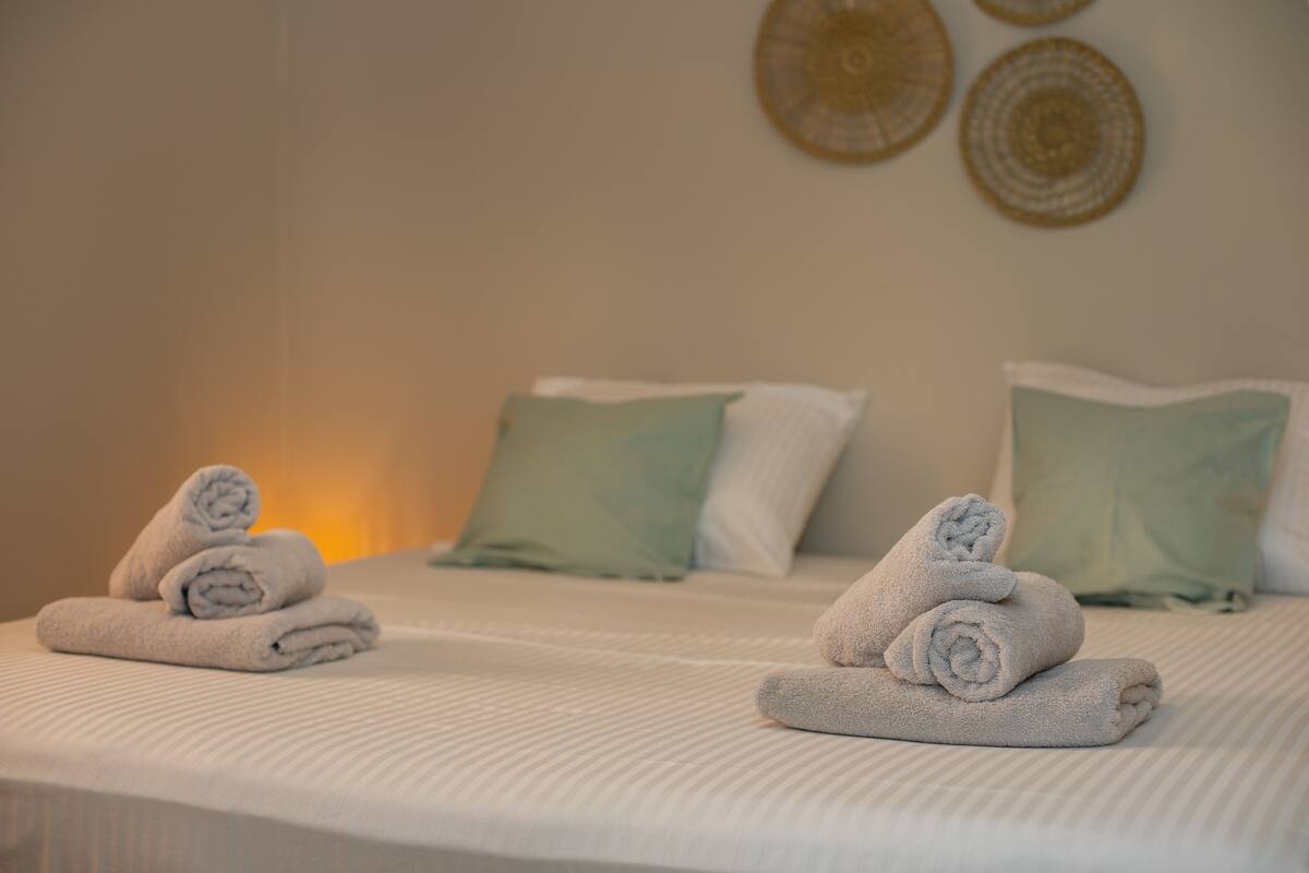 Een net opgemaakt bed met opgerolde handdoeken en lichtgroene kussens.