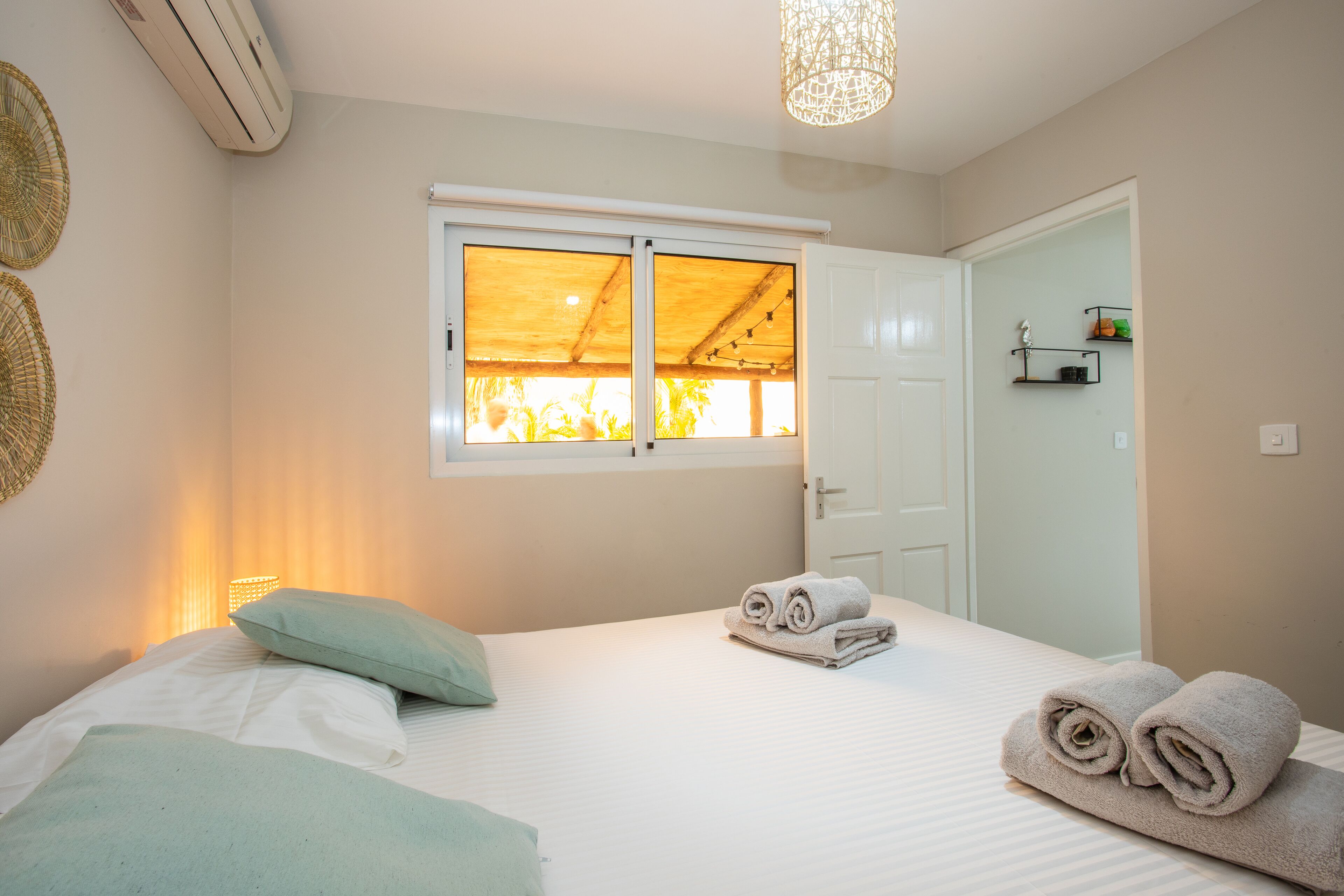 A bedroom with a bed, a window, a door, and a wall-mounted shelf.