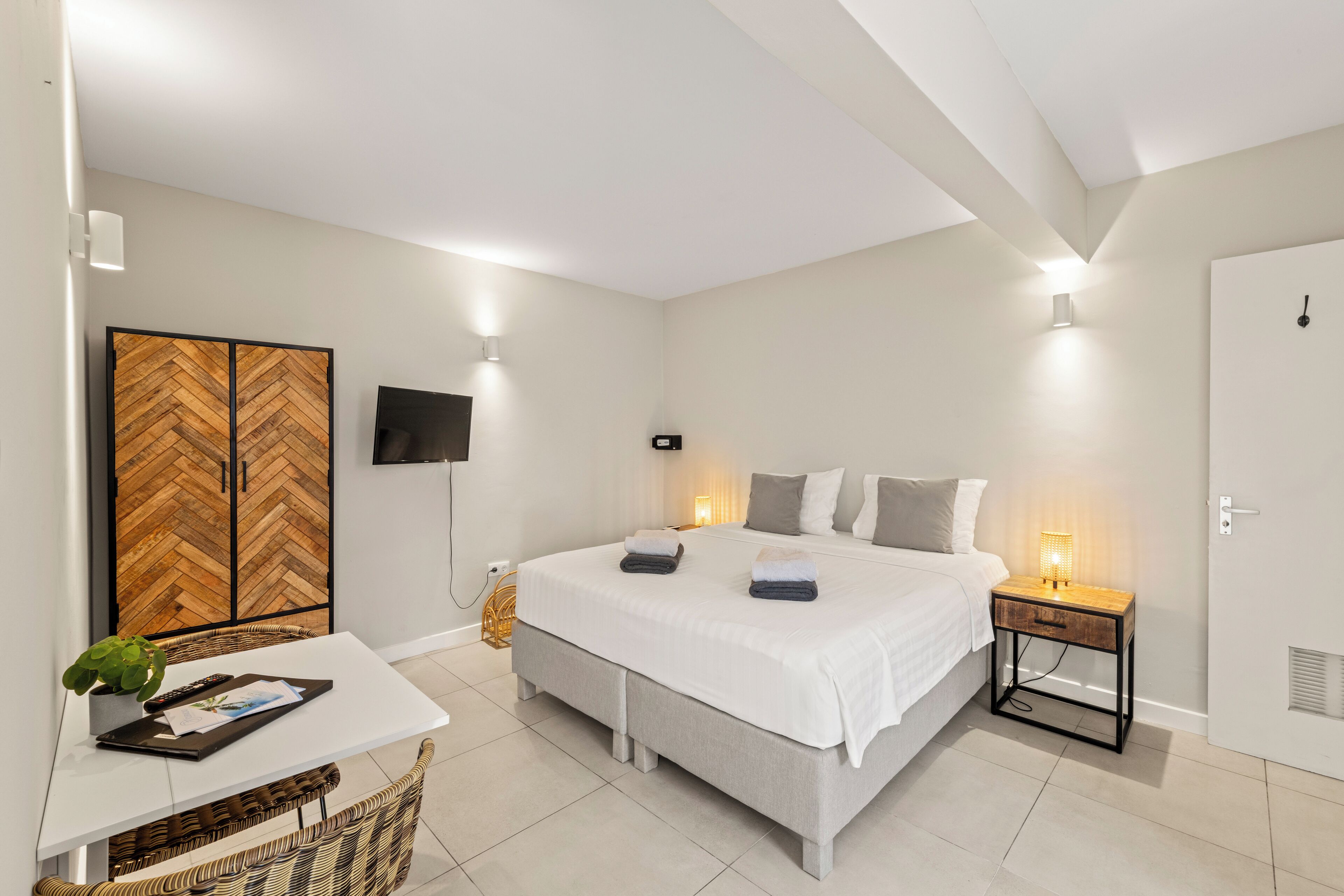 A modern bedroom with a large bed, bedside tables, a TV, and a herringbone-patterned wardrobe.