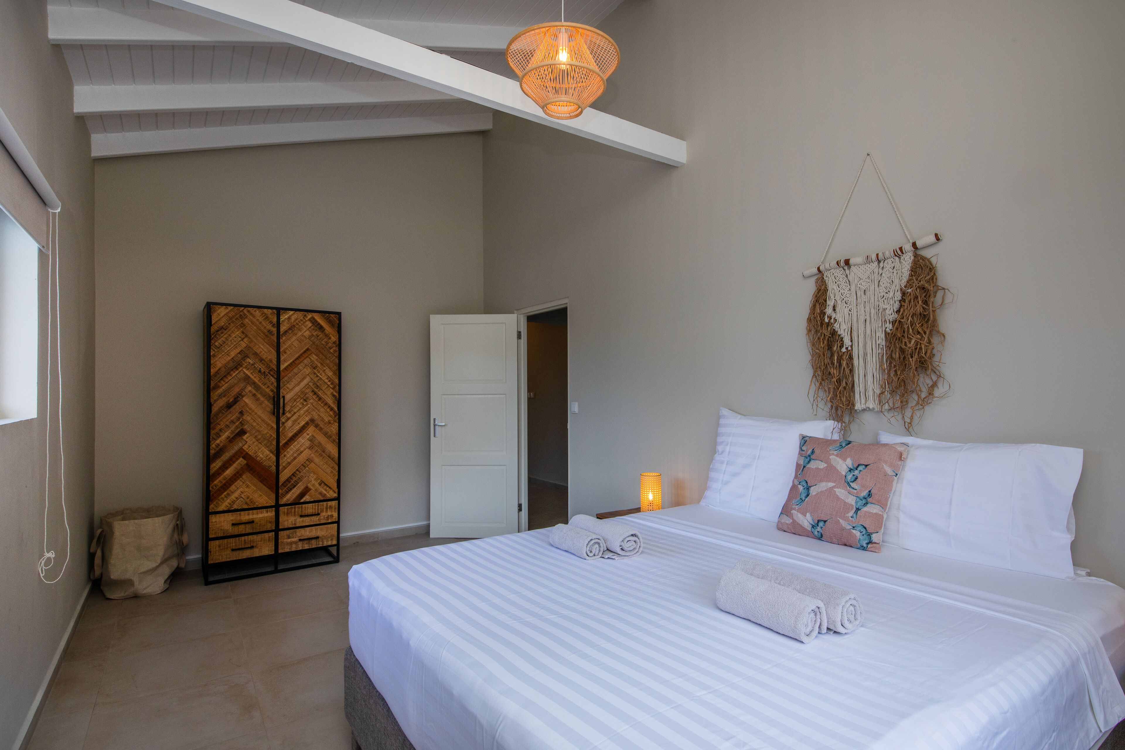 A bedroom with a large bed, a wardrobe, a hanging macrame piece, and a hanging light fixture.