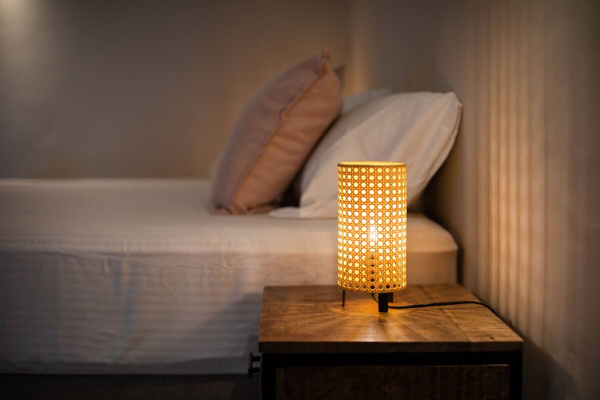 Een bed met een houten nachtkastje en een brandende lamp.