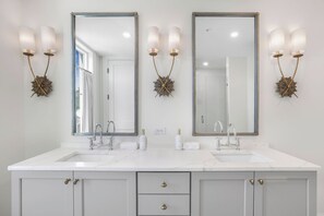 A bathroom with two sinks, a large mirror, and wall sconces. - Luxury Condo Overlooking Downtown Fairhope #201 (Fairhope)