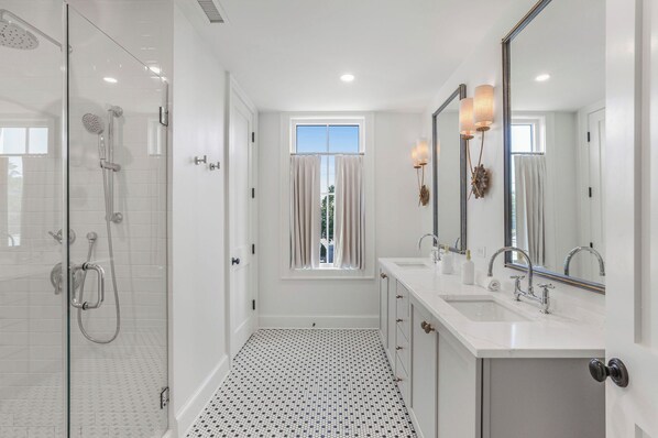 A modern bathroom with a glass-enclosed shower, a large vanity with dual sinks, and a large mirror with wall sconces.