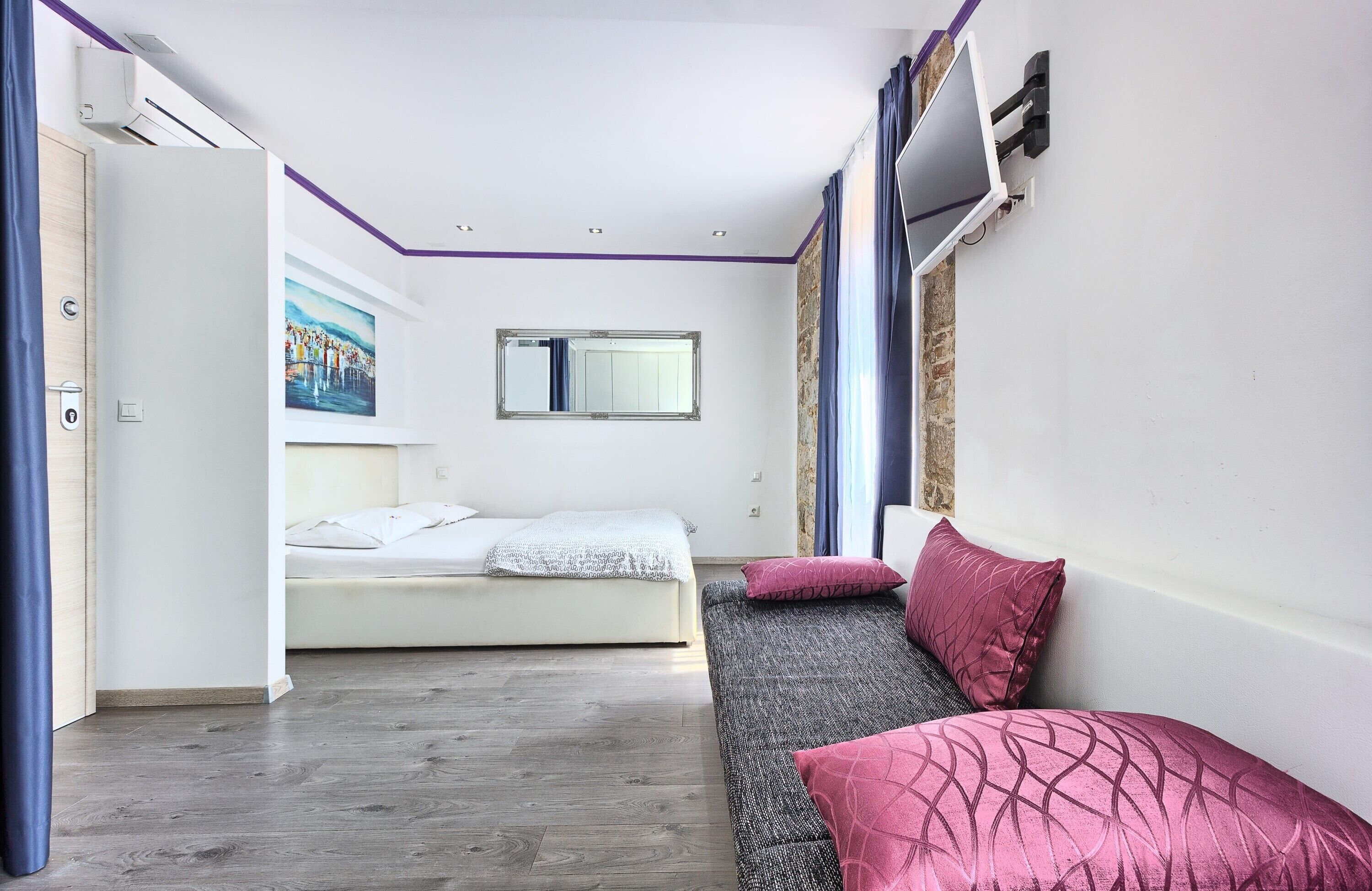 Ein modernes Schlafzimmer mit Bett, Sofa, Fenster und einem Bild an der Wand.