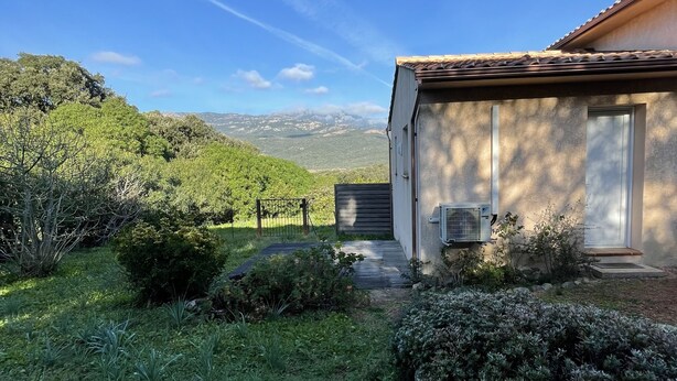A house with a tiled roof, a small garden with various plants, and a view of distant hills. - Studio Figari, au Calme Avec Magnifique vue sur la Montagne et les Vignes (Figari)