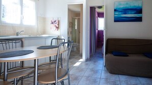 A compact kitchen with a dining area, a sofa, and a view into the living room. - Studio Figari, au Calme Avec Magnifique vue sur la Montagne et les Vignes (Figari)