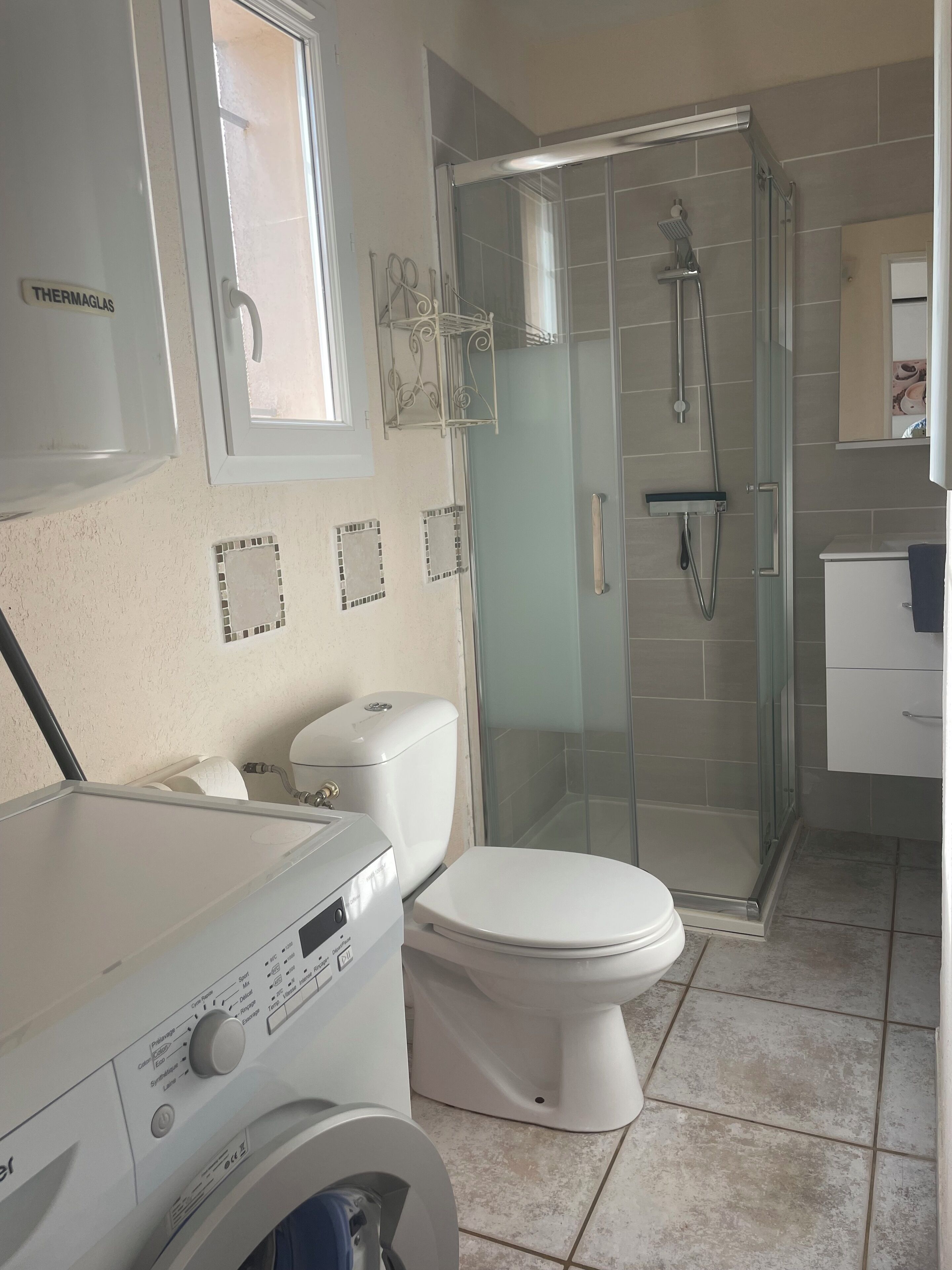 A bathroom with a toilet, a washing machine, and a glass-enclosed shower area.