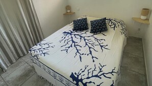 A bedroom with a bed, a window, a wall hanging, and a bedside table. - Studio Figari, au Calme Avec Magnifique vue sur la Montagne et les Vignes (Figari)