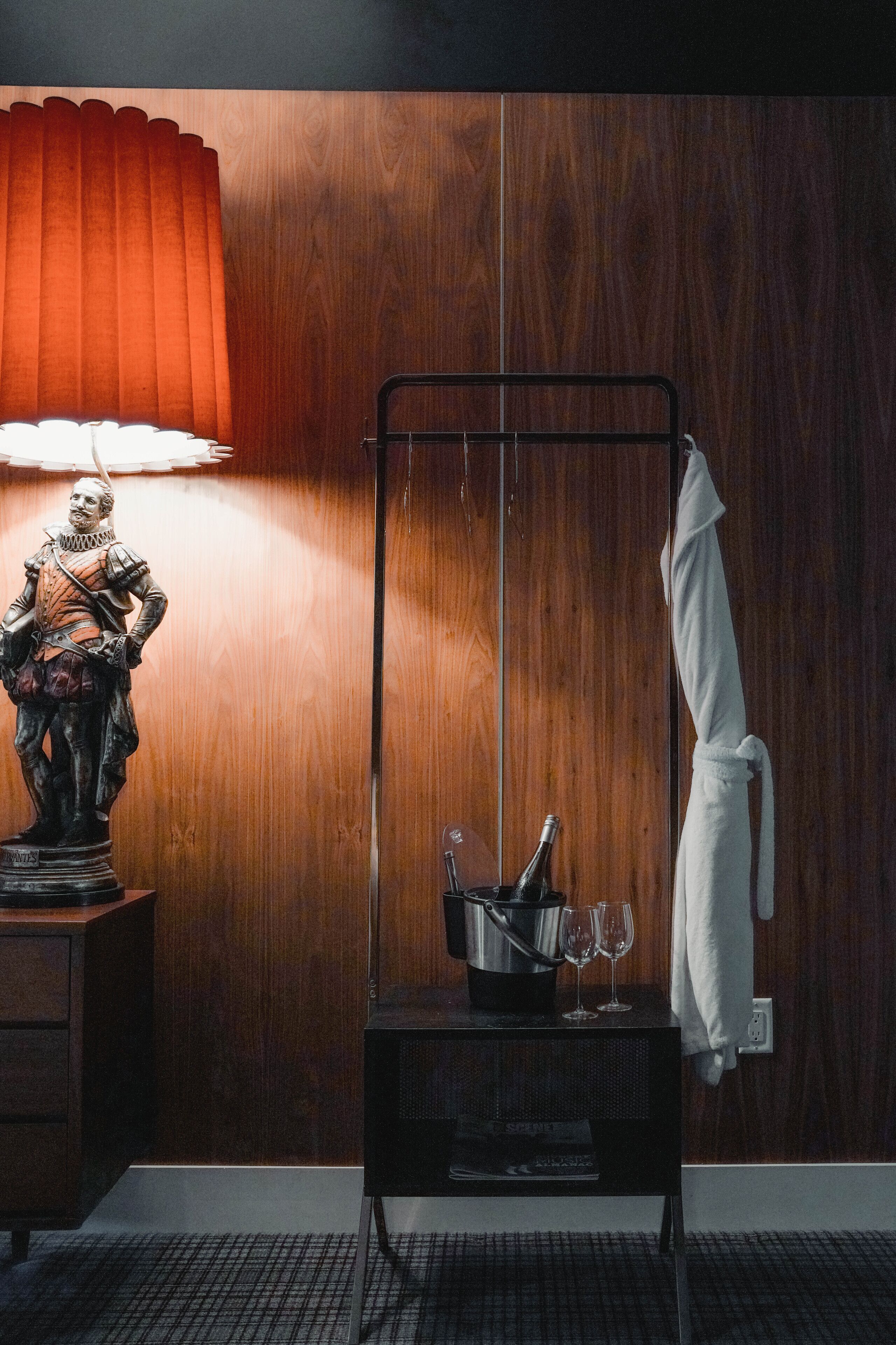 Un baño con pared de madera, un estante metálico con una toalla, una estatua y una lámpara.