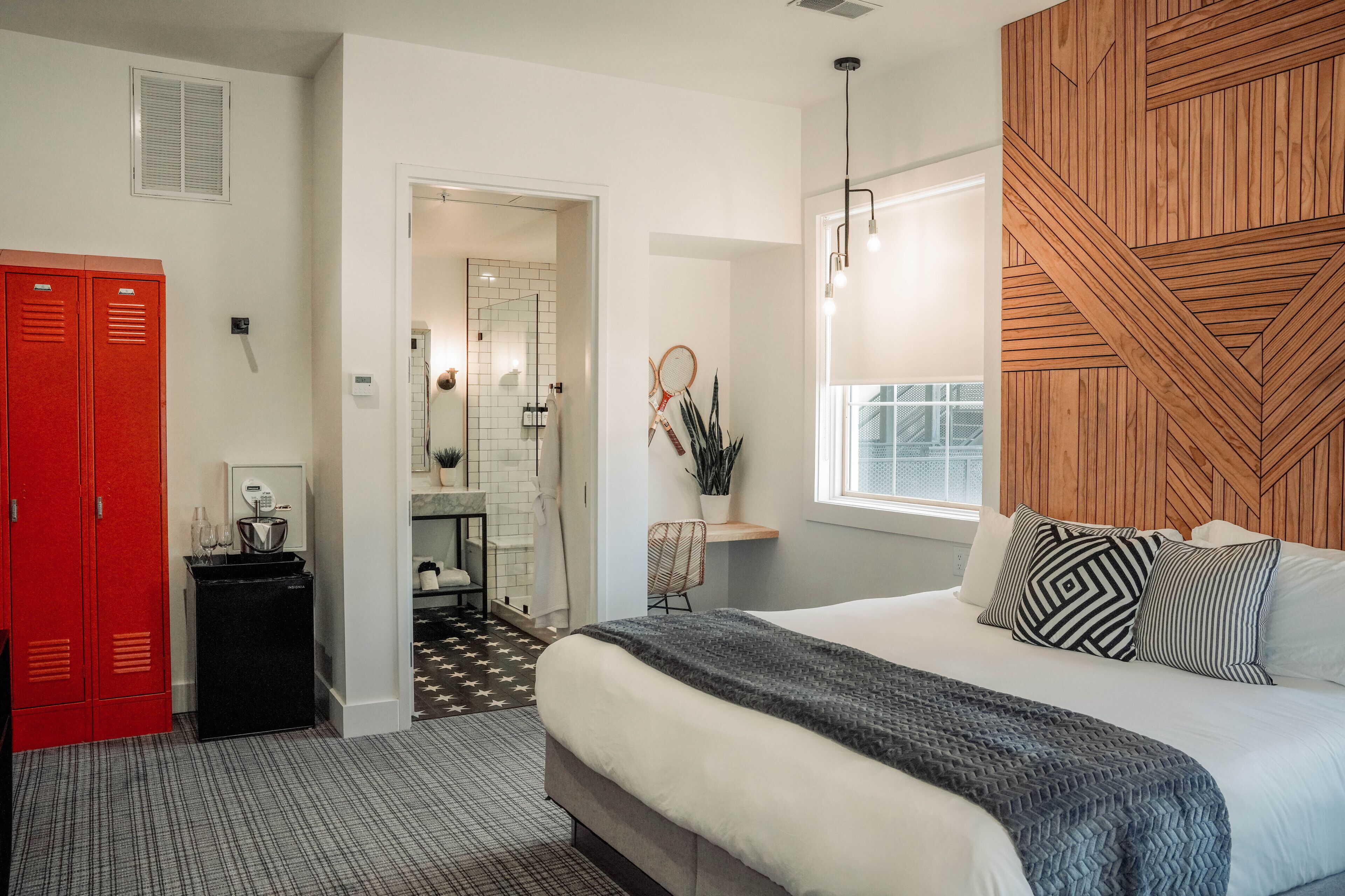 A bedroom with a bed, a wooden headboard, a nightstand, a red wardrobe, and a bathroom visible through an open door.