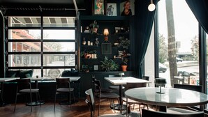 A cozy cafe with wooden floors, multiple tables and chairs, and a large window offering a view of the street. - Reunion Hotel (Nashville)