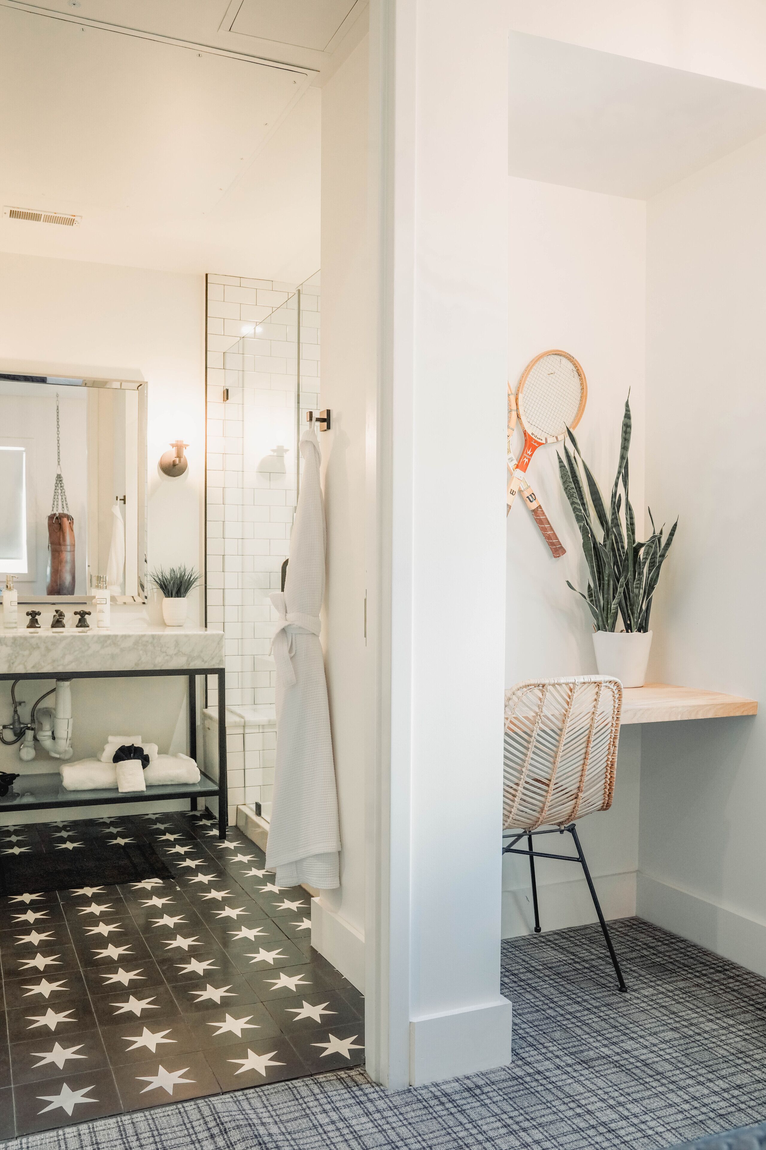 A modern bathroom with a white sink, mirror, and towel rack. There is a shower area with a glass door and a potted plant on the floor.