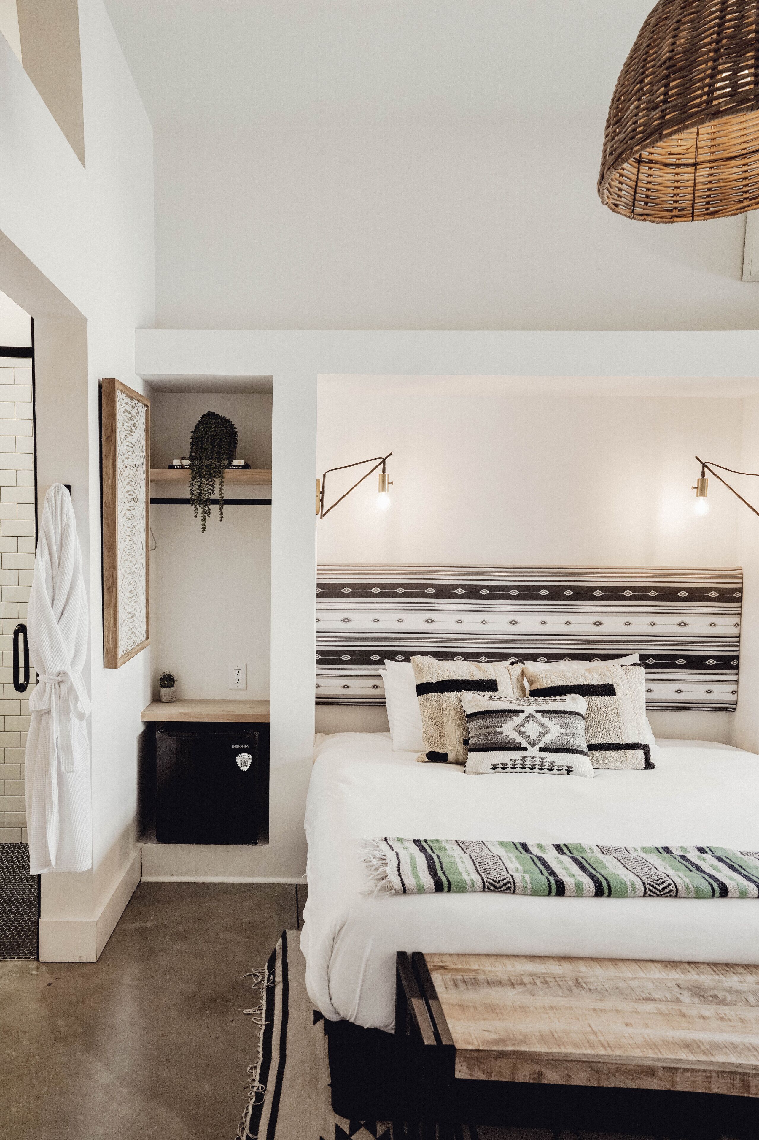 Une chambre à coucher avec un lit, des tables de chevet, un luminaire suspendu, un peignoir et une petite plante.
