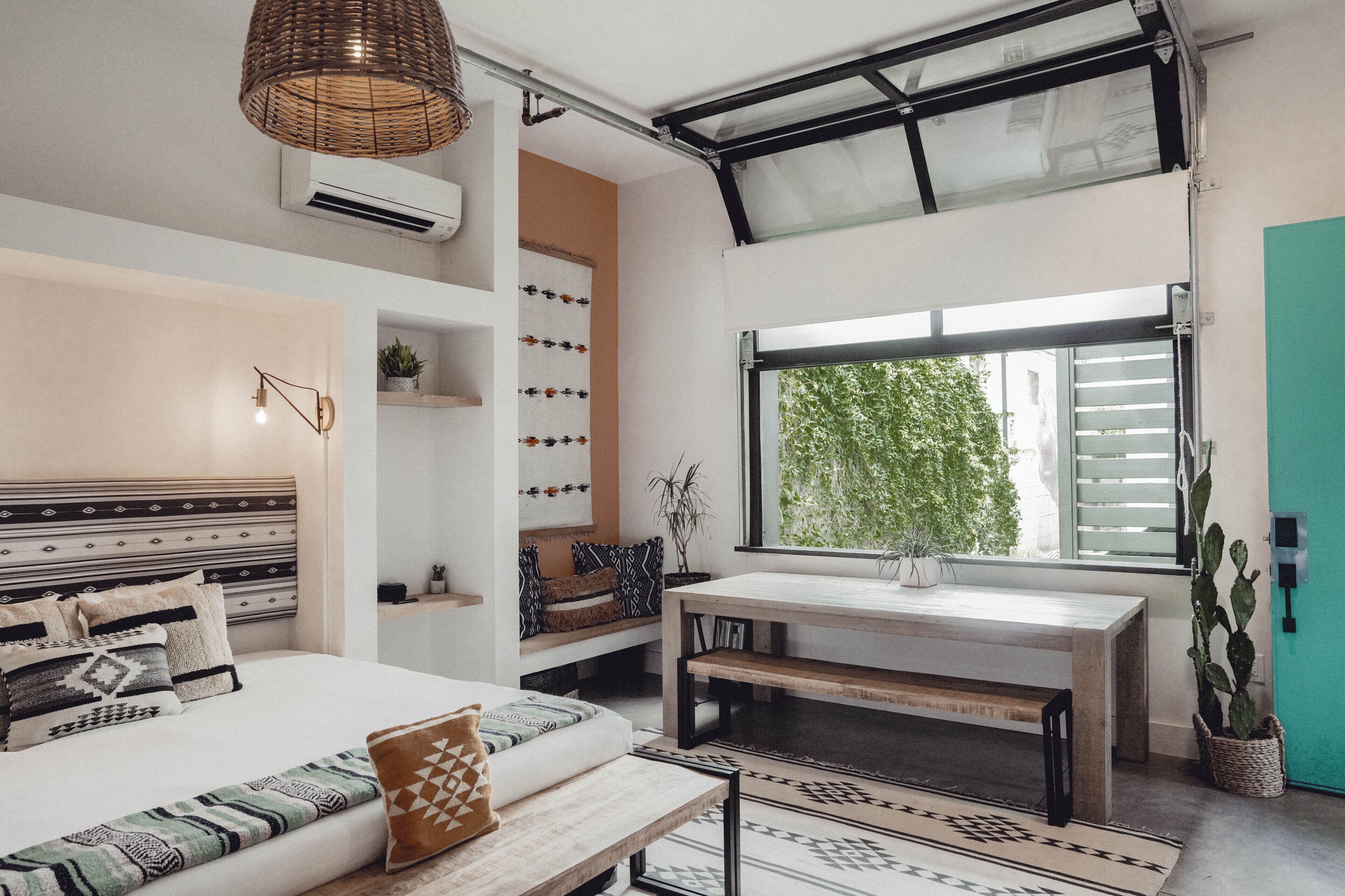 A modern bedroom with a bed, bedside tables, a bench, a window with a view of greenery, and a ceiling fan.