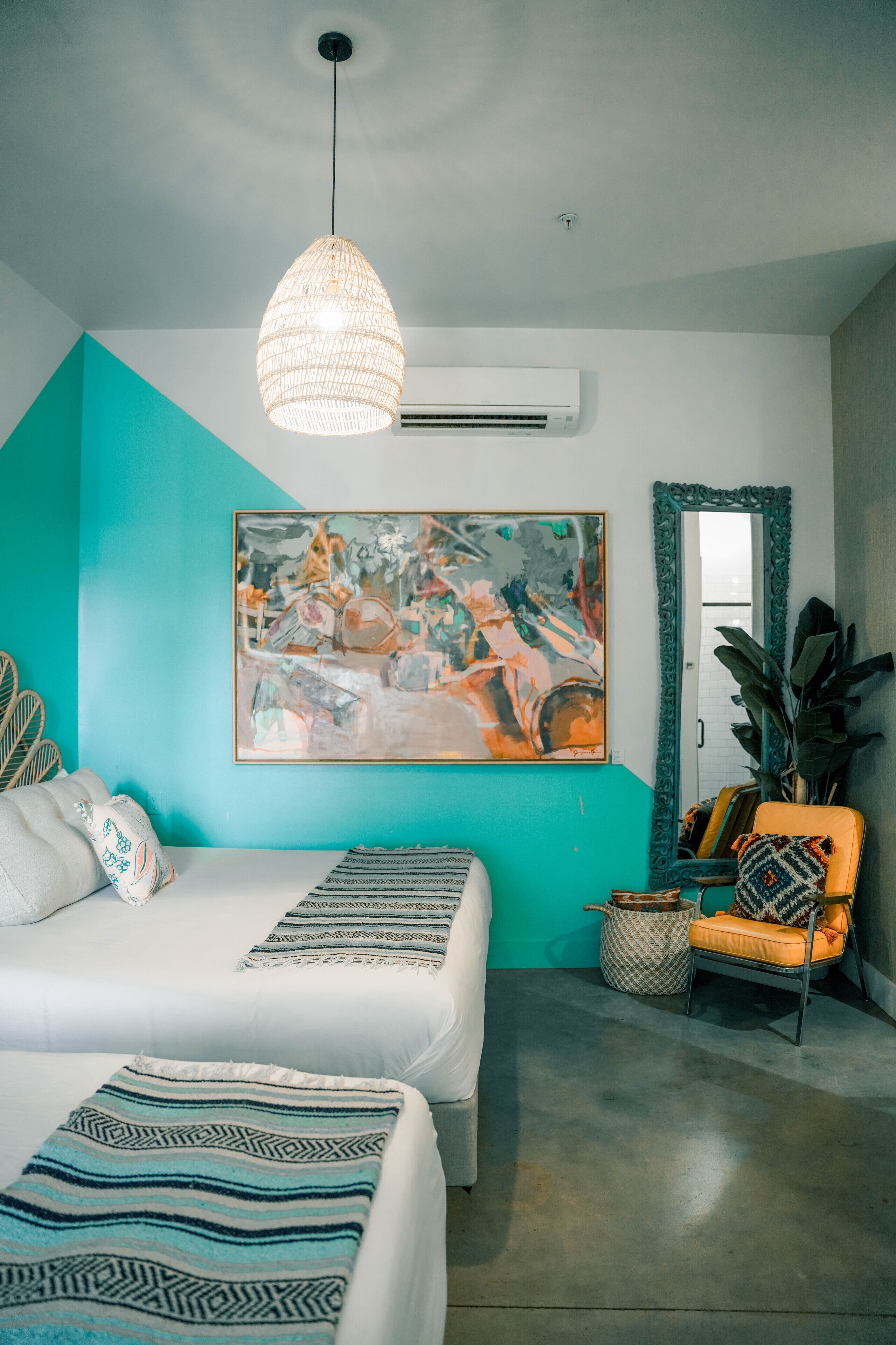 A bedroom with a bed, a chair, a hanging light fixture, and a painting on the wall.
