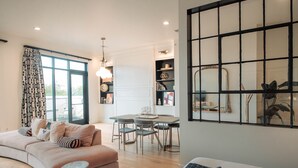A modern living room with a curved sofa, a dining area with a table and chairs, and a large window with patterned curtains. - Reunion Hotel (Nashville)