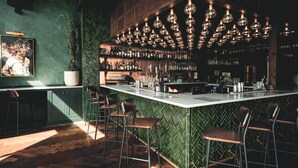Un espace bar avec un mur orné d’un motif en chevrons, un long comptoir avec des tabourets et des luminaires sphériques suspendus.