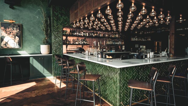 A bar area with a herringbone patterned wall, a long counter with stools, and hanging spherical light fixtures. - Reunion Hotel (Nashville)