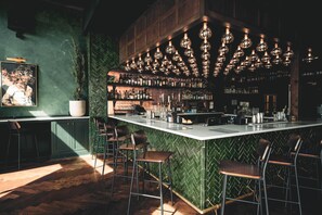 A bar area with a herringbone patterned wall, a long counter with stools, and hanging spherical light fixtures.