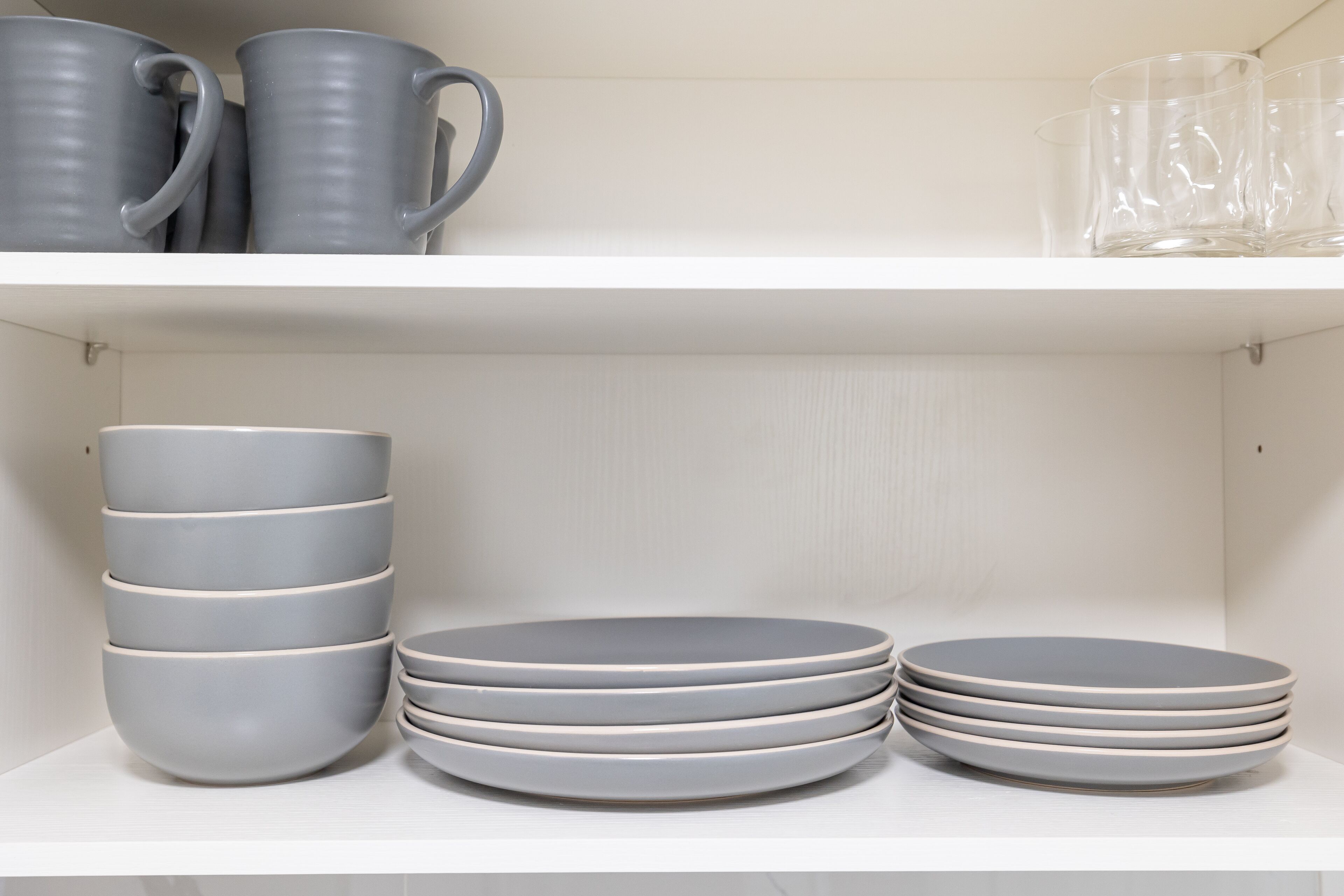Una estantería con tazas grises, platos y vasos.
