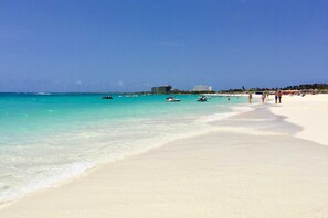 A beach with clear turquoise water, a sandy shore, and a few boats. - Eagle Beach - Sunset Dreams 2BR condo - LV303 (Eagle Beach)