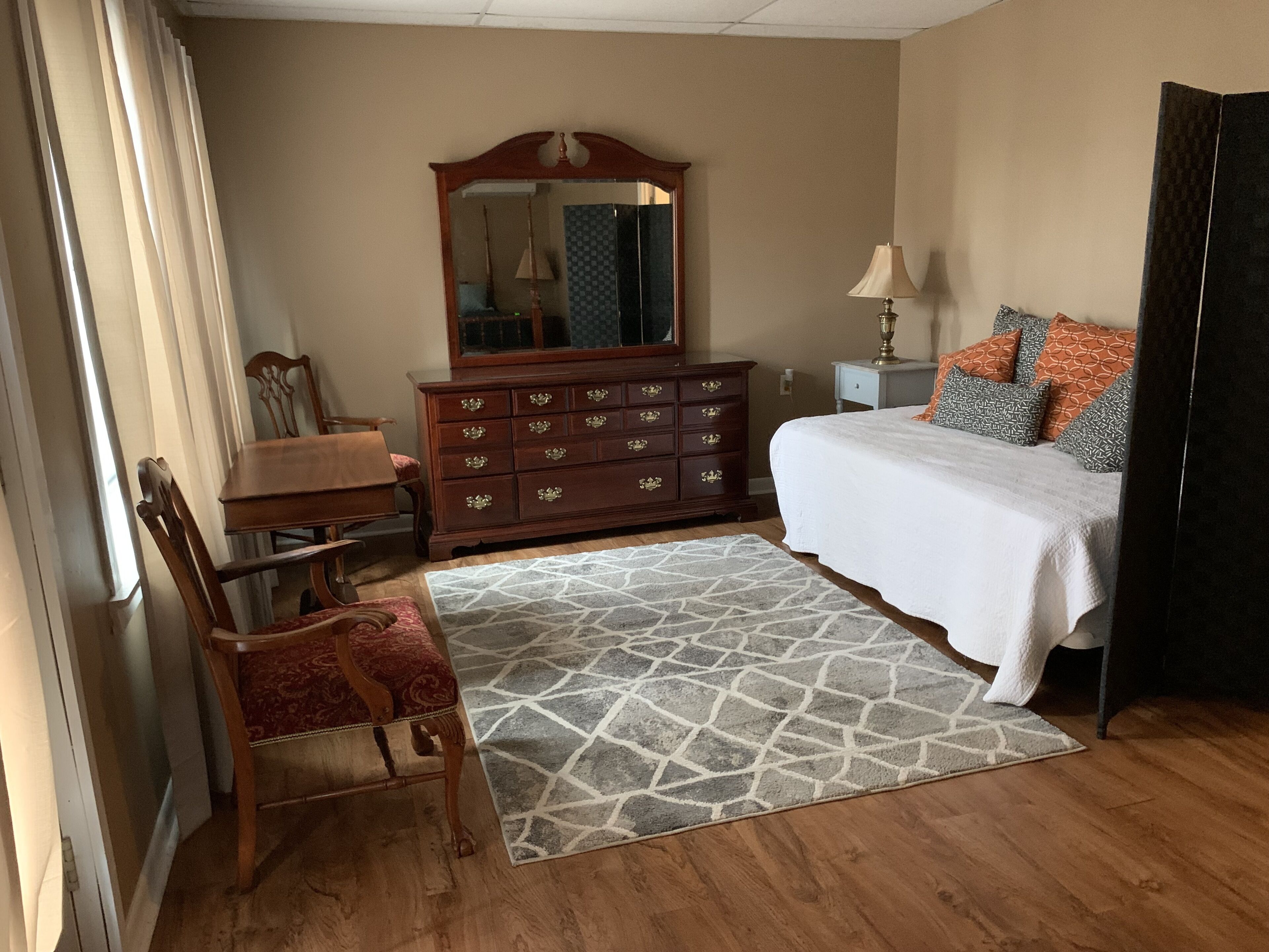 Un dormitorio con un aparador de madera, una cama con almohadones estampados, una mesita de noche y una silla.