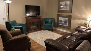 A living room with a fireplace, a television, two armchairs, a sofa, and two framed pictures on the wall. - Aunt Minnie's Peabody Flat near Mountain View's Historic Courthouse Square (Mountain View)