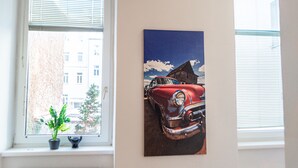 Ein Zimmer mit Fenster, einer Topfpflanze und einem Gemälde eines Oldtimers.
