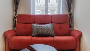 Ein rotes Sofa mit einem gemusterten Kissen in einem Zimmer mit Fenster und Vorhängen.