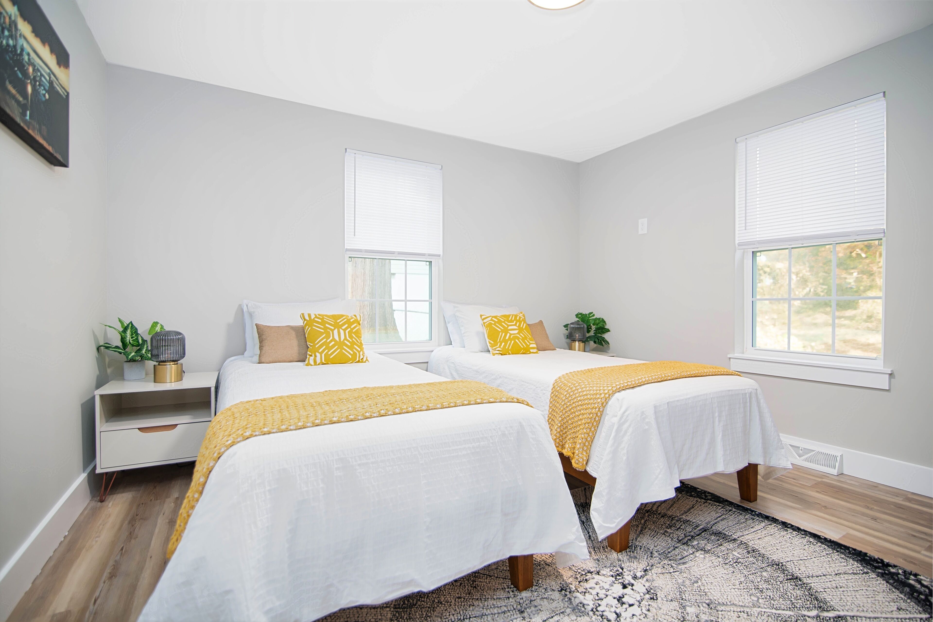 A bedroom with two beds, a nightstand, a window, and a plant.