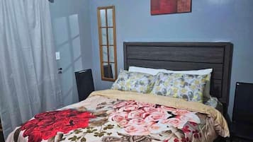 A bedroom with a bed, a window, a door, and a painting on the wall.